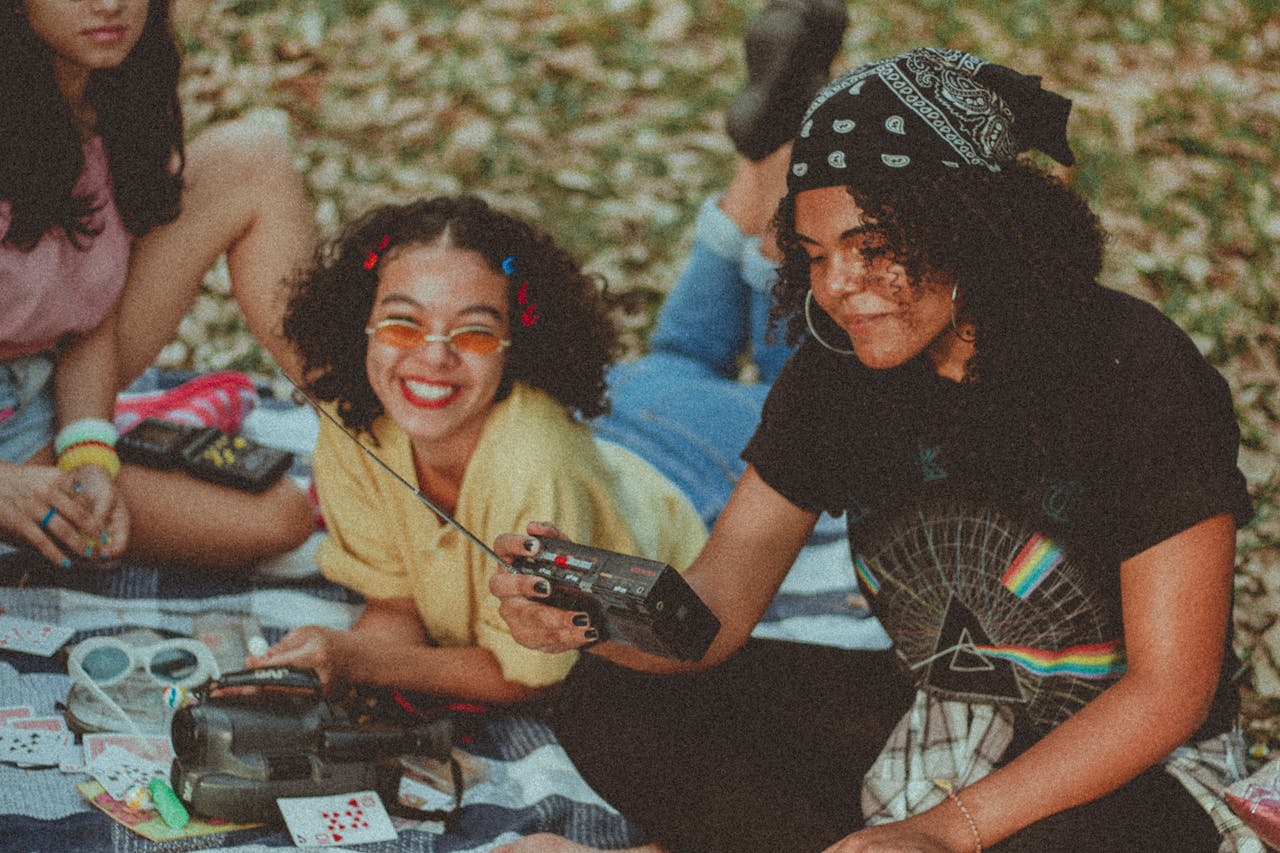 Three women having fun with a vintage radio at an outdoor picnic, embodying retro style and cheerful friendship.